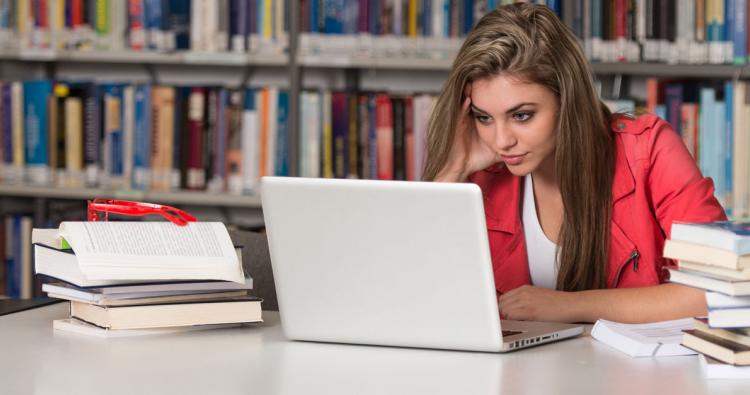 Junge Frau lernt in einer Bibliothek mit ihrem Laptop