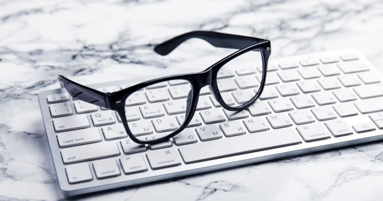 schwarze Brille auf Apple Tastatur auf weißem Marmor