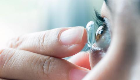 Kundin hält weiche Kontaktlinse auf ihrer Fingerspitze vor das Auge.