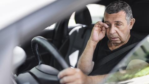 Ein älterer Herr am Steuer eines Autos reibt sich die Augen.