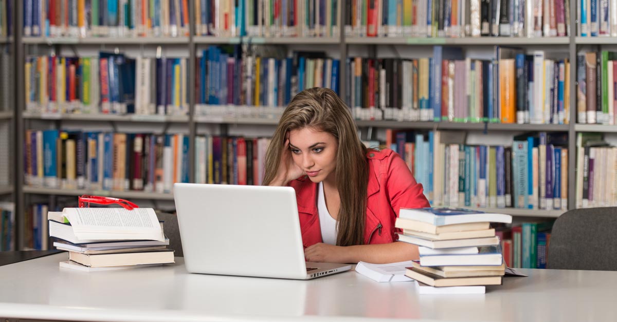 Junge Frau sitzt vor ihrem Laptop und Büchern