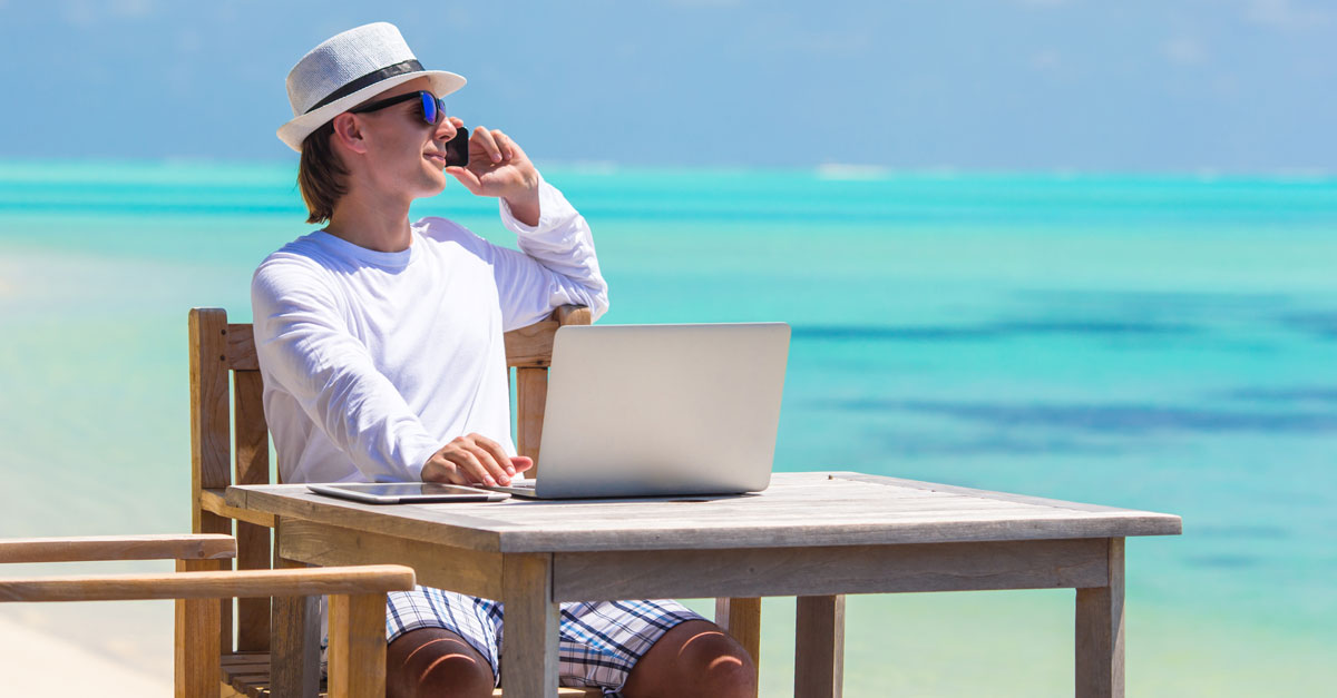 telefonierender Mann sitzt mit Laptop am Strand