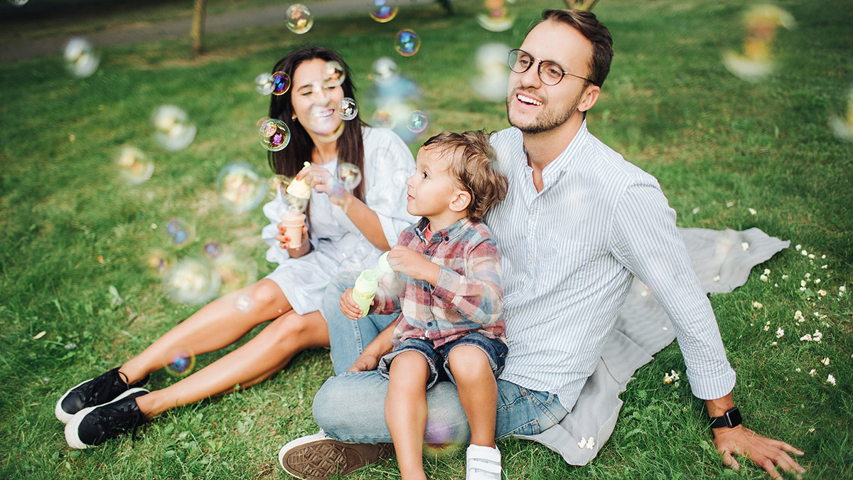 Familie sitzt auf der Wiese und pustet Luftblasen