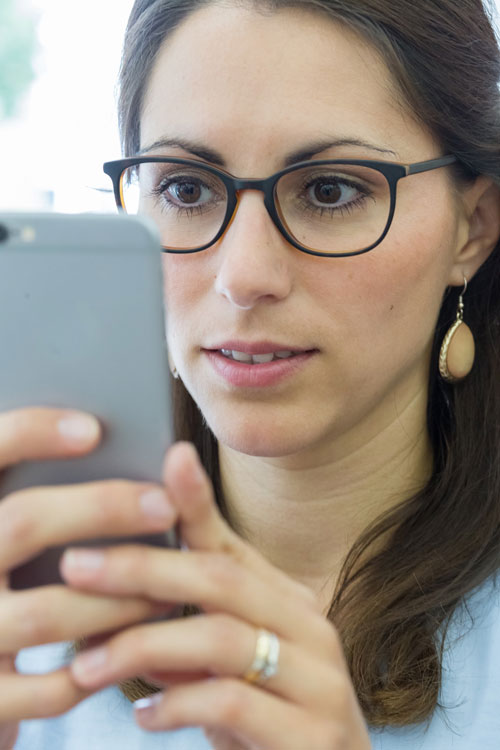 Brillenträgerin schaut auf ihr Smartphone