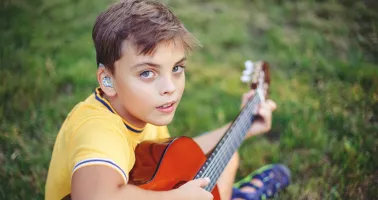 Kind mit Hörgerät spielt Gitarre