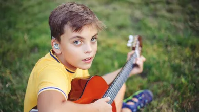 Kind mit Hörgerät spielt Gitarre