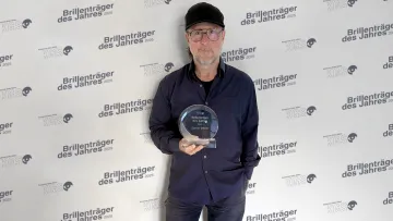 Mann mit Basecap und Brille hält eine Auszeichnung in der Hand