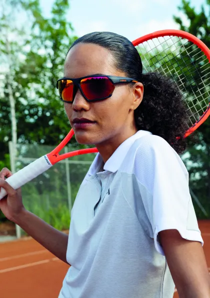 Frau mit Sportsonnenbrille und Tennisschläger auf der Schulter