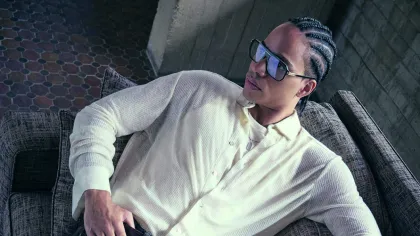 Mann mit Sonnenbrille und weißem Hemd sitzt auf einem Sofa
