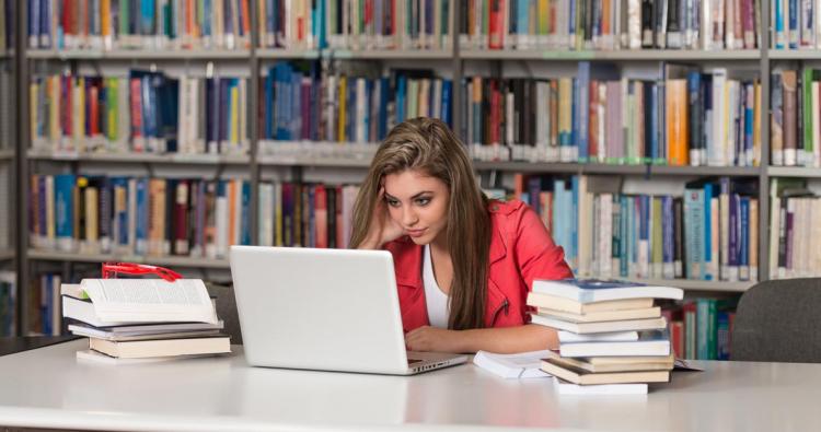 Junge Frau sitzt vor ihrem Laptop und Büchern