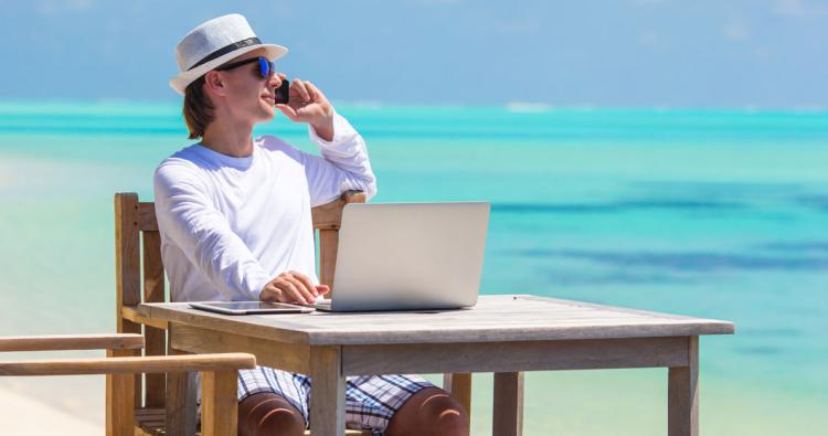 telefonierender Mann sitzt mit Laptop am Strand