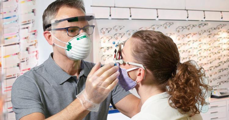 Augenoptiker refraktioniert mit Maske und Visier während Corona