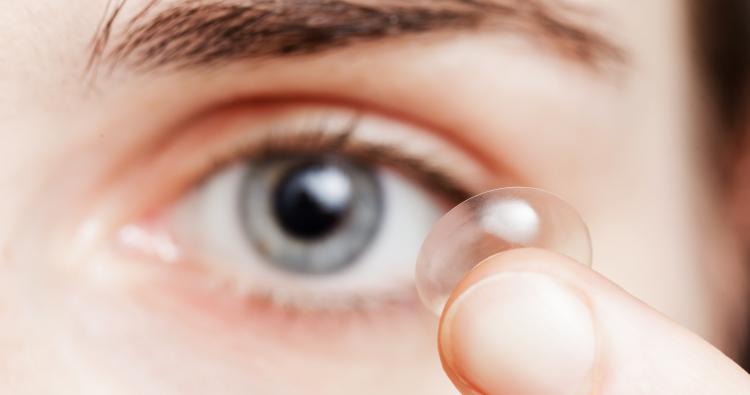 Eine Frau hält sich eine Kontaktlinse vor das Auge.