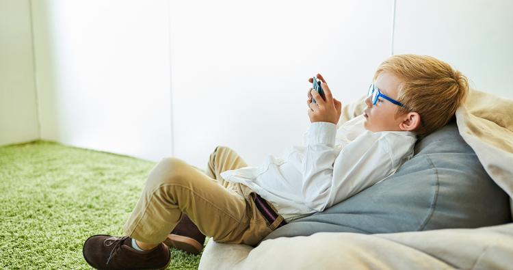 Ein kleiner Junge mit Brille schaut auf ein Smartphone Display.