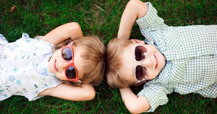 zwei Kinder mit Sonnenbrillen im Gras liegend