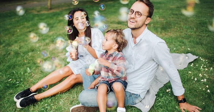 Familie sitzt auf der Wiese und pustet Luftblasen