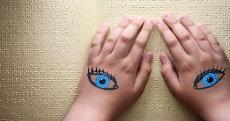 Hände mit aufgemalten Augen auf Papier mit Brailleschrift