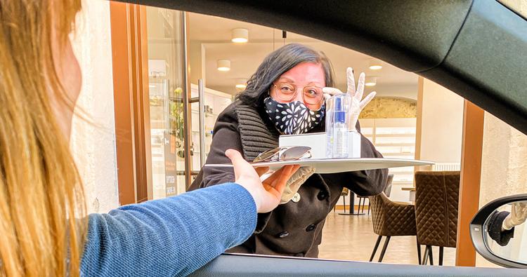 Frau mit Mundschutz reicht Tablett ins Auto 