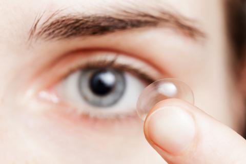 Eine Frau hält sich eine Kontaktlinse vor das Auge.