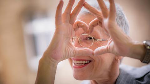 Lächelnde Brillenträgerin formt Herz mit Händen