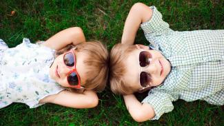 zwei Kinder mit Sonnenbrillen im Gras liegend