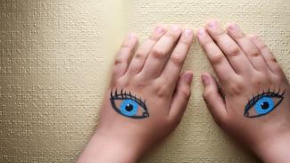 Hände mit aufgemalten Augen auf Papier mit Brailleschrift