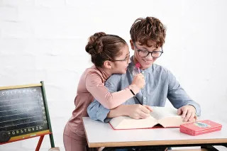 Junge und Mädchen mit Brille am Tisch mit Buch