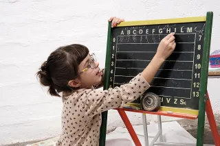 kleines Mädchen mit Brille malt etwas an die Tafel