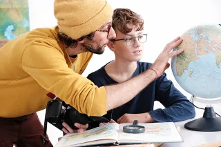 Fotograf zeigt Jungen mit Brille etwas auf dem Globus